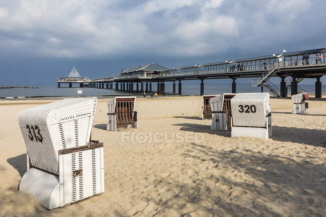Germany, Mecklenburg-Western Pomerania, Heringsdorf, Hooded beach chairs on sandy coastal beach with pier in background — Stock Photo