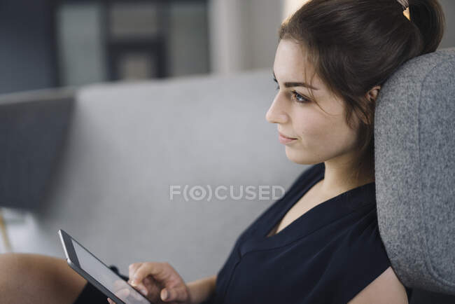Jeune femme d'affaires assise sur le canapé avec tablette numérique regardant à distance — Photo de stock