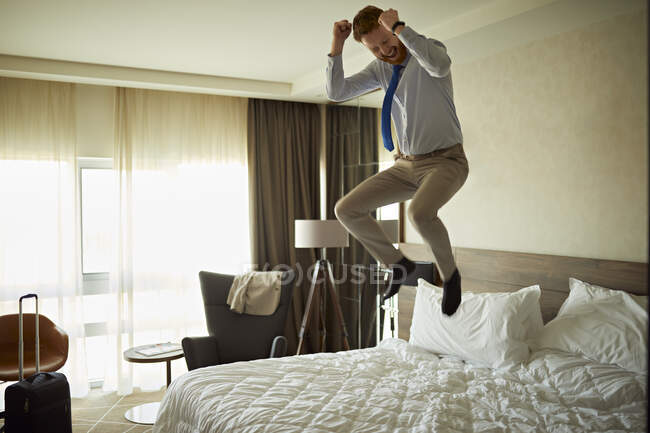 Eccitato uomo d'affari che salta sul letto in camera d'albergo — Foto stock