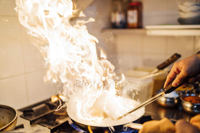 Indian chef flambing food in restaurant kitchen, close up — Stock Photo