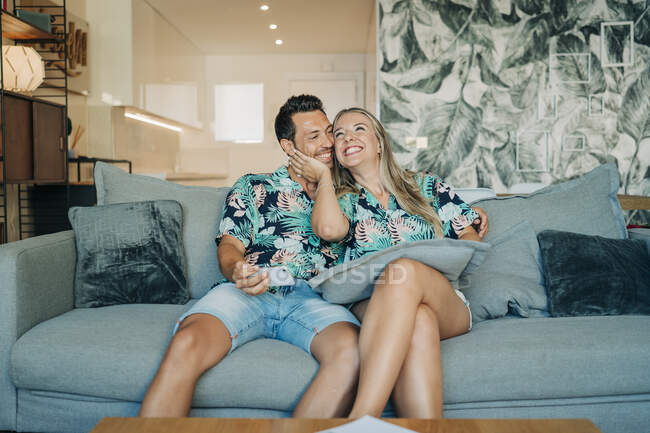 Счастливая пара сидит на диване в гостиной в гавайских рубашках — стоковое фото