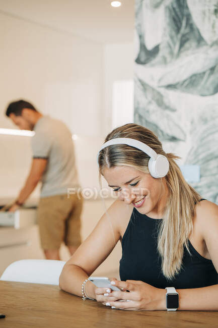 Smiling woman sitting at table with headphones and smartphone — Stock Photo