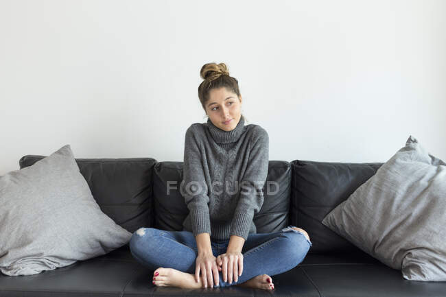 Ritratto di giovane donna seduta sul divano di pelle nera guardando la distanza — Foto stock