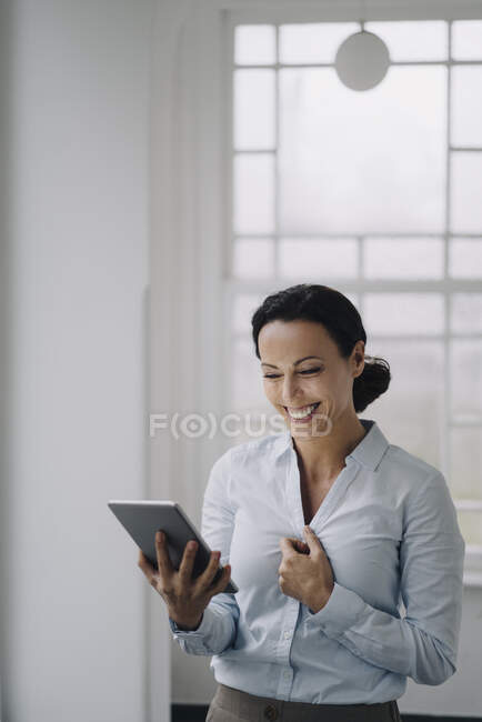 Успішна комерсантка стоїть біля вікна, користується цифровим планшетом, усміхається — стокове фото