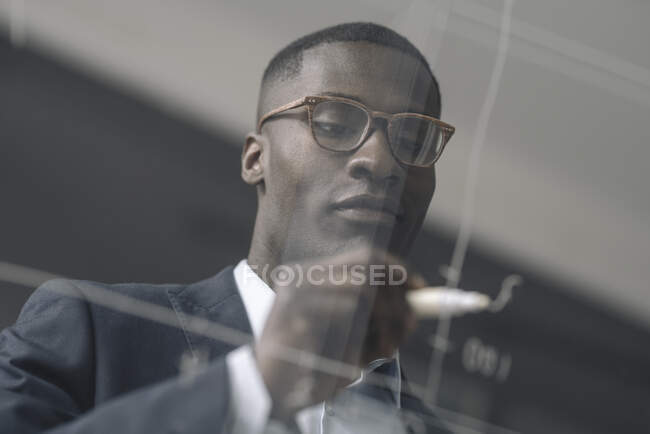 Porträt eines jungen Geschäftsmannes zeichnet Diagramm auf Glasscheibe im Büro — Stockfoto