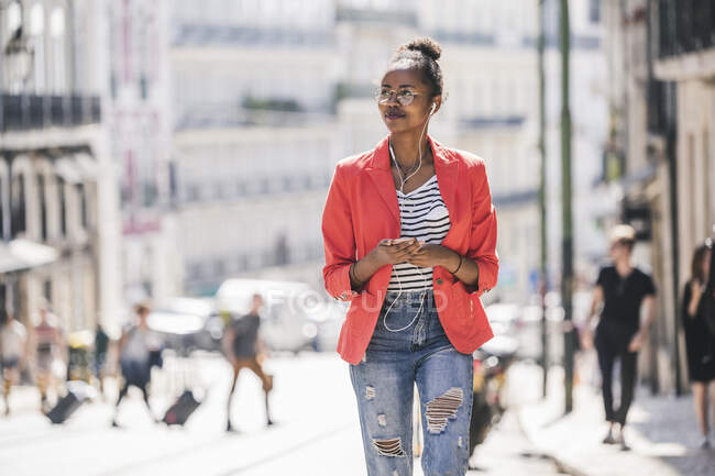 Giovane donna con auricolari e smartphone che si guarda intorno in città, Lisbona, Portogallo — Foto stock