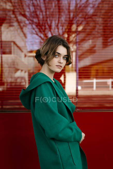 Young woman wearing green coat in front of a red glass pane — Stock Photo