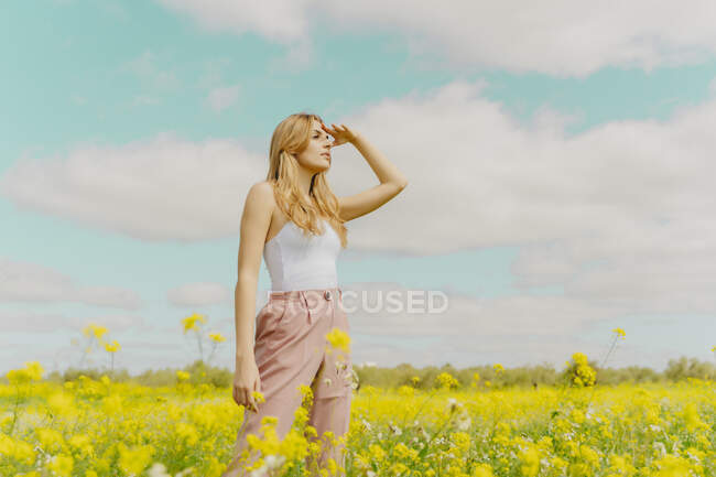 Young woman standing in a flower meadow in spring looking out — Stock Photo