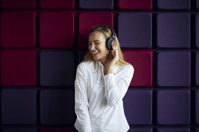 Ritratto di donna felice a un muro viola ascoltando musica con le cuffie — Foto stock