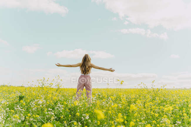 Vista trasera de la joven mujer de pie en un prado de flores en primavera con los brazos extendidos - foto de stock