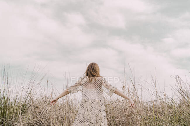 Вид ззаду жінки в вінтажному одязі з витягнутими руками на віддаленому полі в сільській місцевості — стокове фото