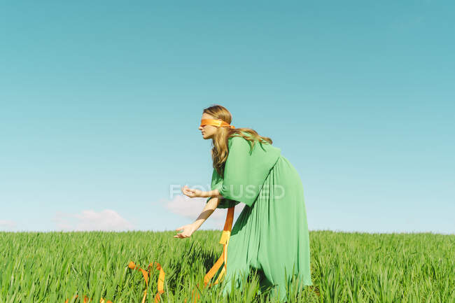 Giovane donna bendata che indossa un vestito verde in piedi in un campo — Foto stock