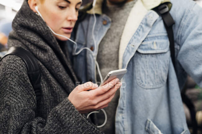Coppia giovane con auricolari utilizzando smartphone su una metropolitana — Foto stock