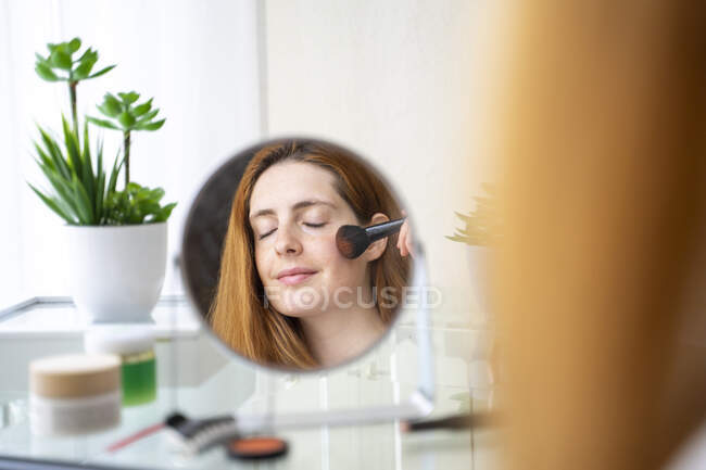 Jeune femme appliquant maquillage à la maison — Photo de stock