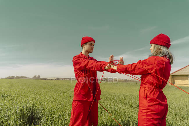 Young couple wearing red overalls and hats performing on a field with red string — Stock Photo