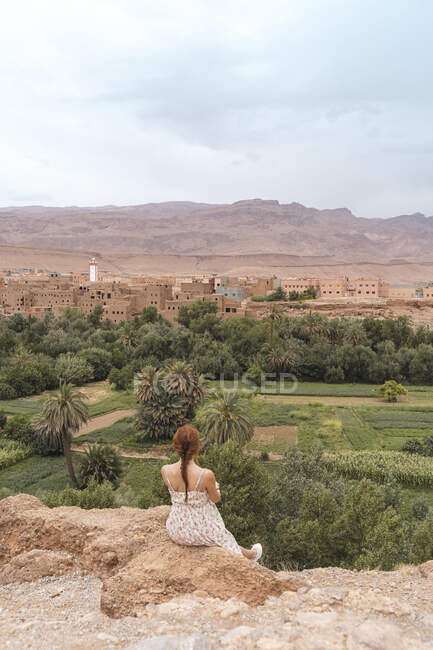 Back view of young womansitting on a rock looking at the city, Ouarzazate, Morocco — Stock Photo