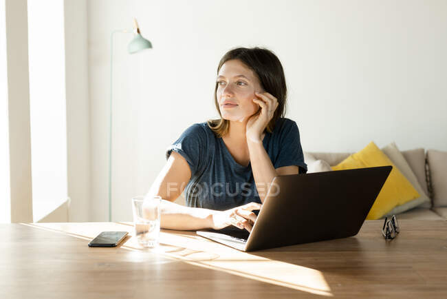Young woman at home working at laptop in home office in modern living room and looking outside — Stock Photo