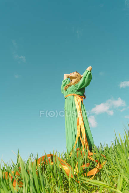 Giovane donna che indossa un abito verde in piedi in un campo con nastri avvolti intorno alla vita — Foto stock
