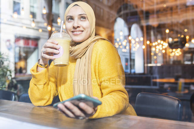 Portrait of young woman with smoothie and smartphone in a cafe — Stock Photo