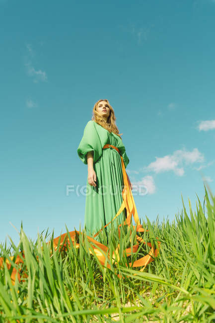 Young woman wearing a green dress standing in a field with ribbons wrapped around her waist — Stock Photo