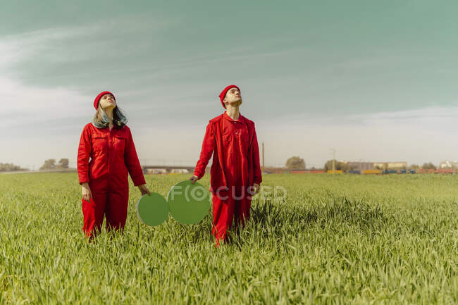 Giovane coppia che indossa tuta rossa in piedi su un campo con due cerchi verdi guardando in alto — Foto stock