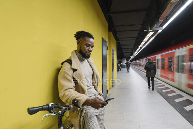 Elegante hombre con bicicleta y smartphone en una estación de metro - foto de stock