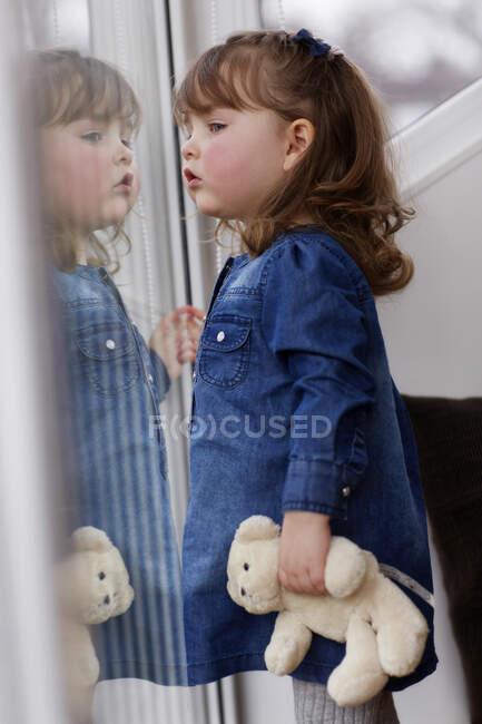 Portrait of curios toddler girl with teddy bear watching something — Stock Photo