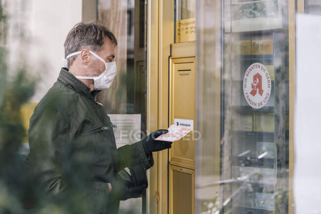 Человек в маске ждет перед аптекой с рецептом — стоковое фото