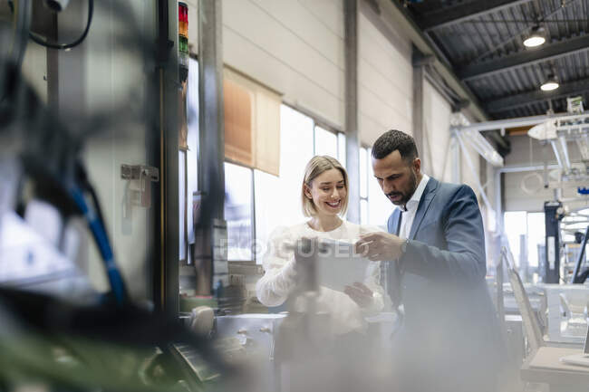 Businessman and young woman with papers talking at a machine in a factory — Stock Photo