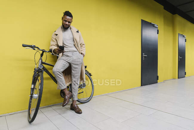 Стильний чоловік з велосипедом і смартфоном біля жовтої стіни — стокове фото