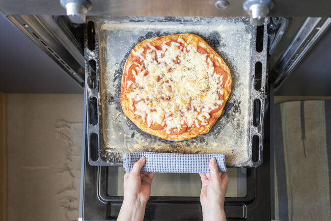 Woman's hands taking tray with baked pizza out of oven — Stock Photo