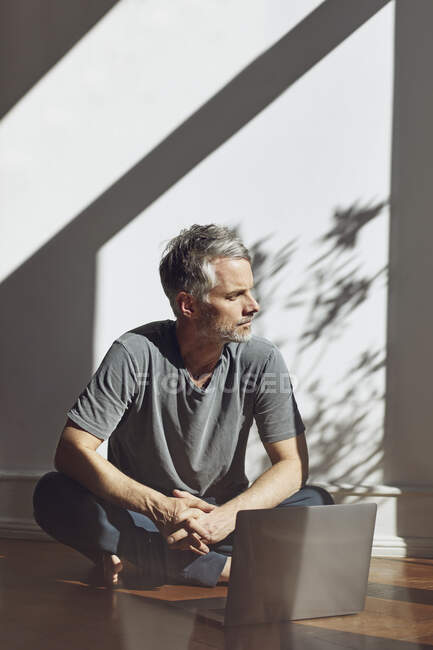 Mature man sitting on the floor with laptop looking at distance — Stock Photo