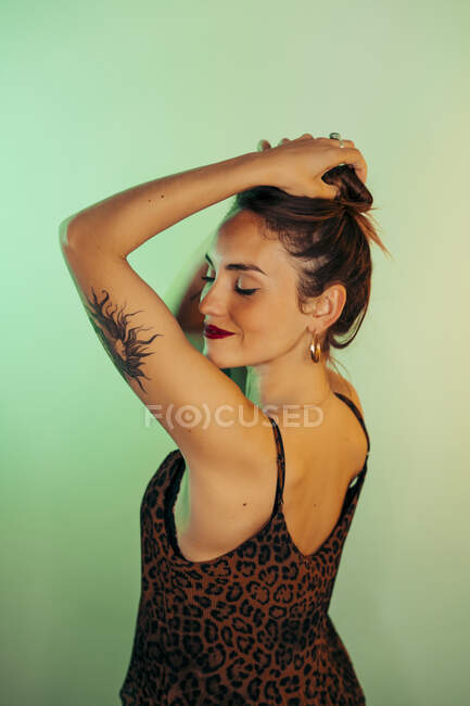 Retrato de mujer joven tatuada con los ojos cerrados sobre fondo verde - foto de stock