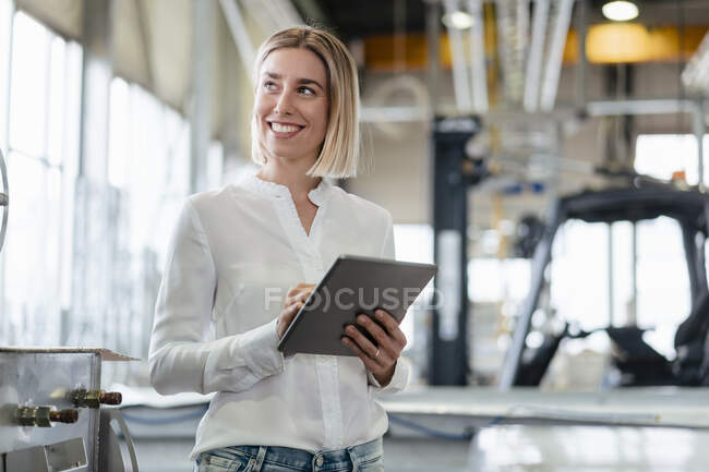 Усміхнена молода жінка використовує планшет на фабриці — стокове фото