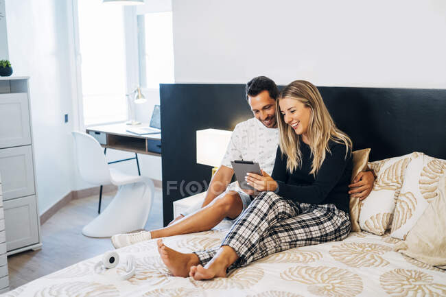 Casal sorridente sentado na cama usando tablet digital para bate-papo por vídeo — Fotografia de Stock