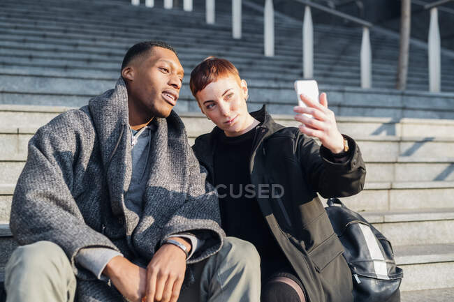 Jeune couple assis dans les escaliers de la ville prenant un selfie — Photo de stock