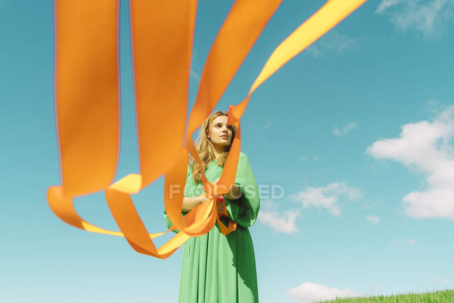 Young woman wearing a green dress holding orange ribbons — Stock Photo