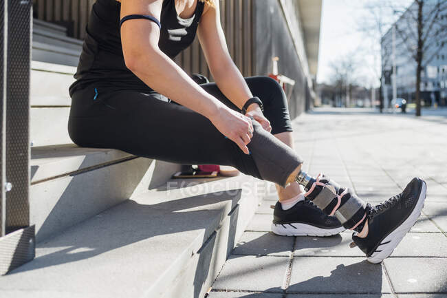 Mujer joven deportiva con prótesis de pierna sentada en las escaleras de la ciudad - foto de stock