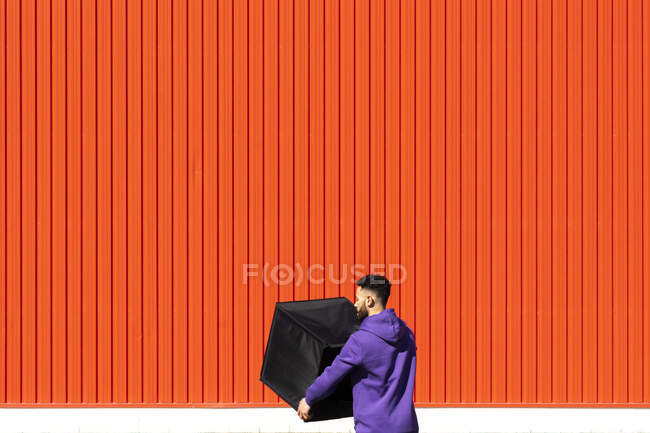 Jovem carregando uma caixa na frente de uma parede vermelha — Fotografia de Stock