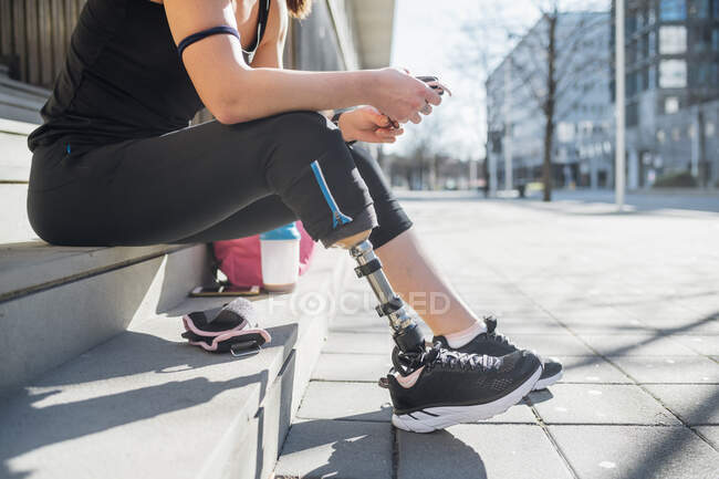 Giovane donna sportiva con protesi alle gambe seduta sulle scale in città utilizzando lo smartphone — Foto stock