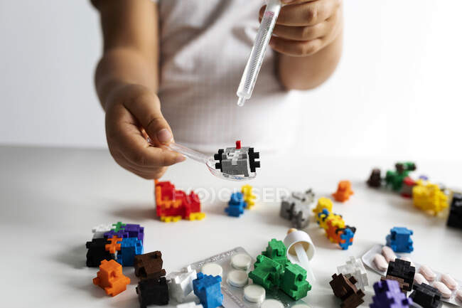 Vista de los cultivos de un niño jugando con bloques de construcción y jeringa durante la cuarentena - foto de stock