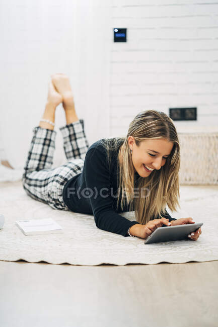 Смеющаяся женщина лежит на полу с помощью мини-планшета — стоковое фото