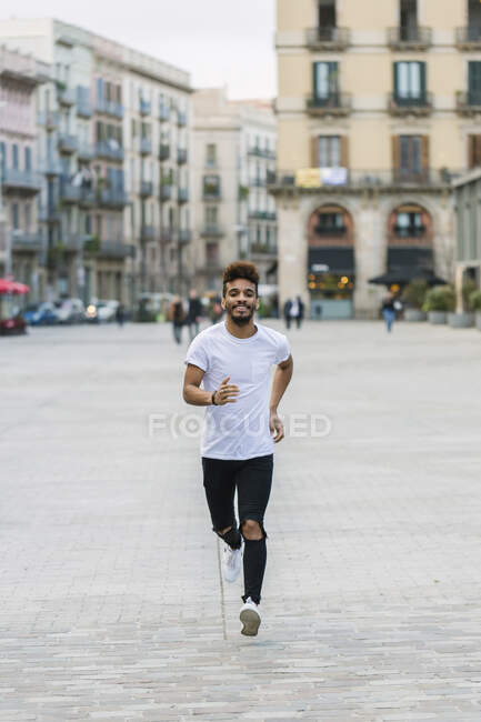 Porträt eines lachenden jungen Mannes, der auf einem Platz läuft, Barcelona, Spanien — Stockfoto
