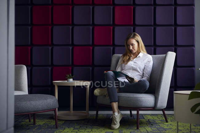 Donna seduta in poltrona nella moderna rivista lounge reading — Foto stock