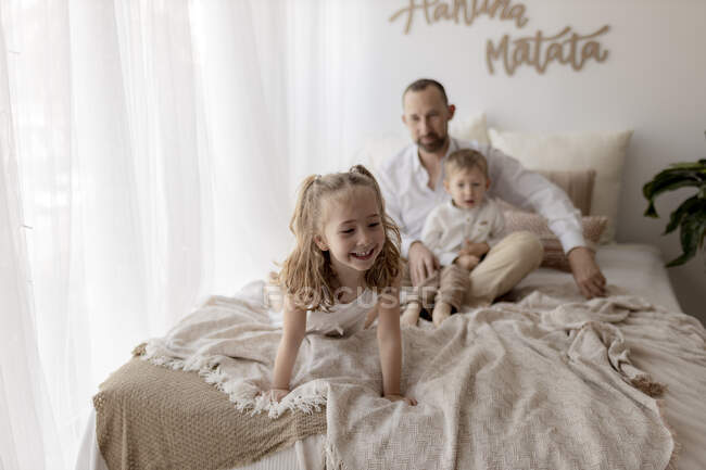 Портрет щасливої маленької дівчинки на ліжку з батьком і братом, який спостерігає за нею з минулого. — стокове фото
