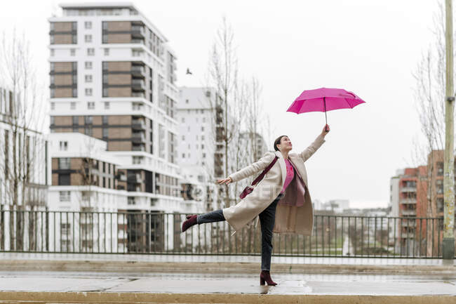 Lächelnde Frau mit rosa Regenschirm spaziert durch die Stadt — Stockfoto
