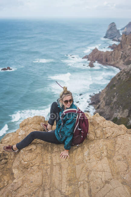 Portugal, Distrito de Lisboa, Sintra, Mochilera sentada al borde del acantilado de Cabo da Roca - foto de stock