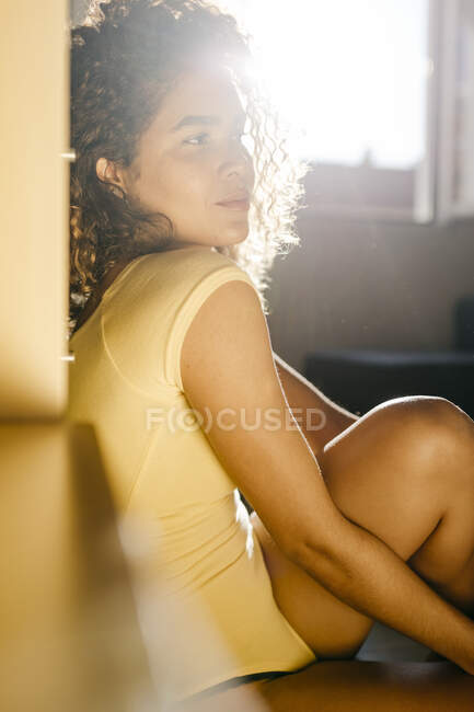 Ritratto di giovane donna attraente seduta sul pavimento a casa alla luce del sole — Foto stock