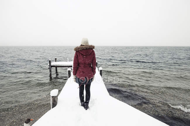 Veduta posteriore di una giovane donna in piedi sul molo innevato del lago Starnberg, Germania — Foto stock