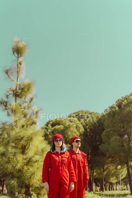 Young couple wearing red overalls and hats standing in nature — Stock Photo